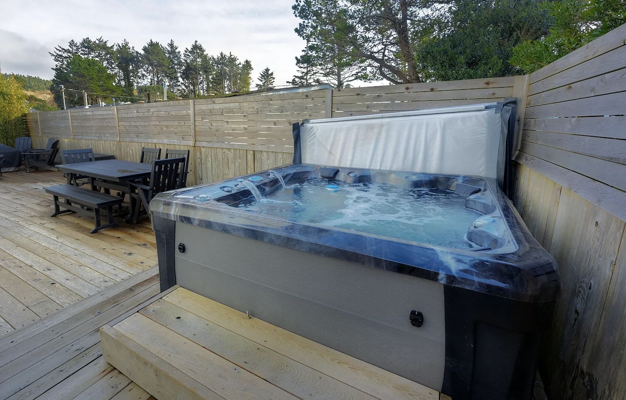 Private hot tub on the fenced back deck, with outdoor dining behind